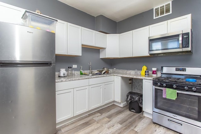 kitchen with stainless steel appliances, visible vents, light wood-style floors, white cabinets, and a sink