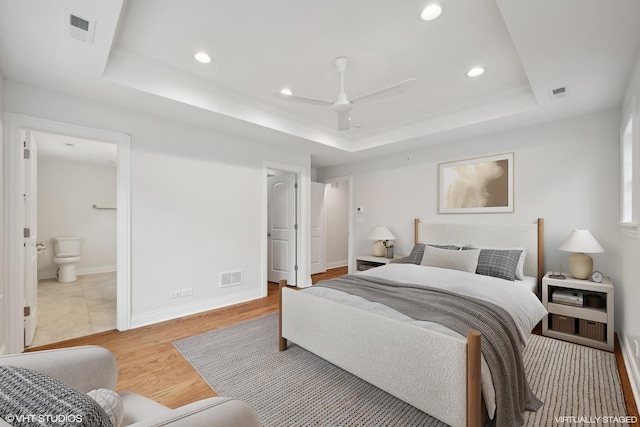 bedroom featuring a tray ceiling, visible vents, and wood finished floors