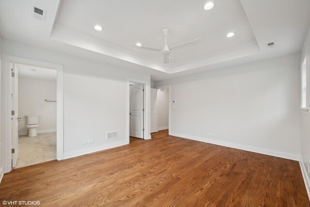 unfurnished bedroom featuring a raised ceiling, visible vents, and light wood-style floors