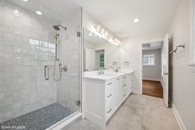 bathroom with double vanity, a shower stall, baseboards, and a sink