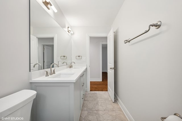 bathroom with baseboards, a sink, toilet, and double vanity