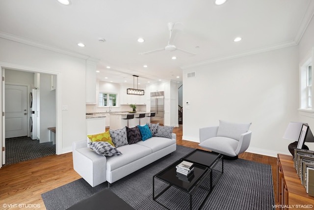 living room featuring light wood-style floors, recessed lighting, visible vents, and ornamental molding