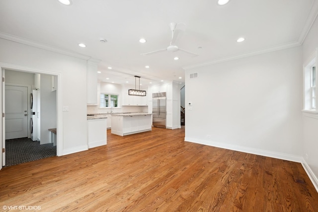 unfurnished living room featuring light wood finished floors, visible vents, ornamental molding, a sink, and baseboards