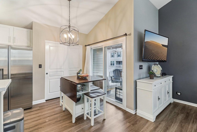 dining space featuring a chandelier, vaulted ceiling, dark wood finished floors, and baseboards