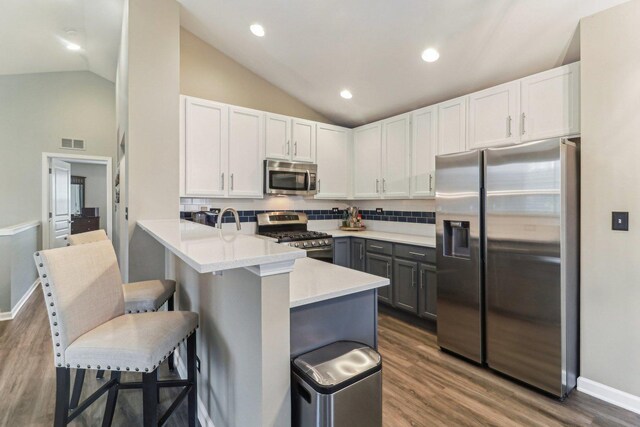 kitchen featuring stainless steel appliances, lofted ceiling, visible vents, a peninsula, and a kitchen bar