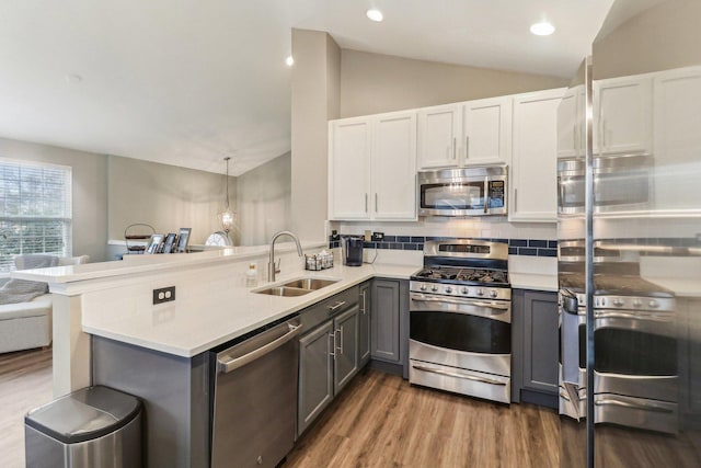 kitchen featuring stainless steel appliances, gray cabinets, a sink, vaulted ceiling, and a peninsula