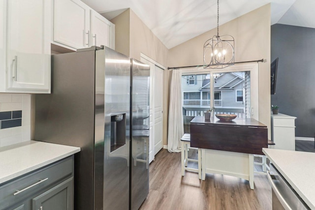 kitchen with stainless steel refrigerator with ice dispenser, tasteful backsplash, lofted ceiling, white cabinetry, and wood finished floors