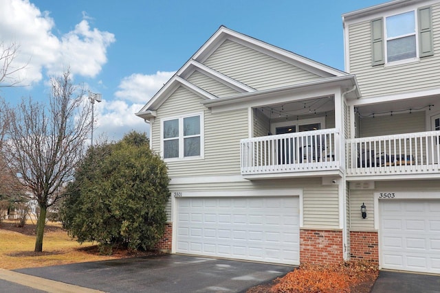 townhome / multi-family property with a garage, driveway, brick siding, and a balcony