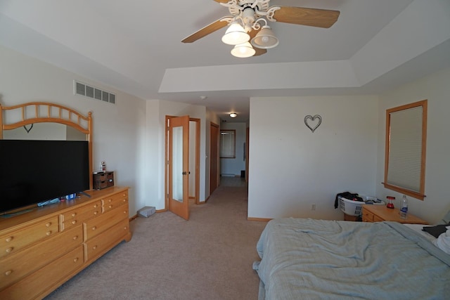 bedroom with a raised ceiling, light colored carpet, visible vents, a ceiling fan, and baseboards