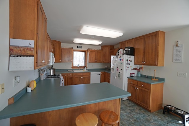 kitchen featuring brown cabinetry, a breakfast bar, white appliances, and a peninsula