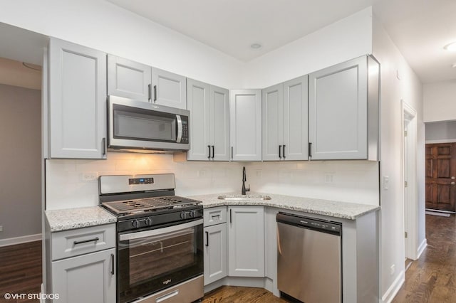 kitchen with a sink, backsplash, dark wood-style floors, appliances with stainless steel finishes, and light stone countertops