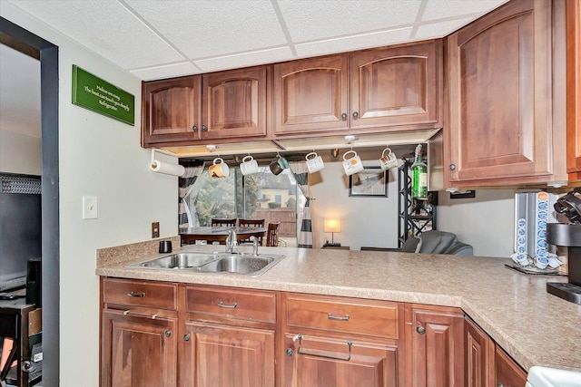 kitchen with brown cabinets, light countertops, a paneled ceiling, and a sink