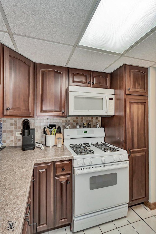 kitchen featuring white appliances, light tile patterned flooring, light countertops, a paneled ceiling, and backsplash