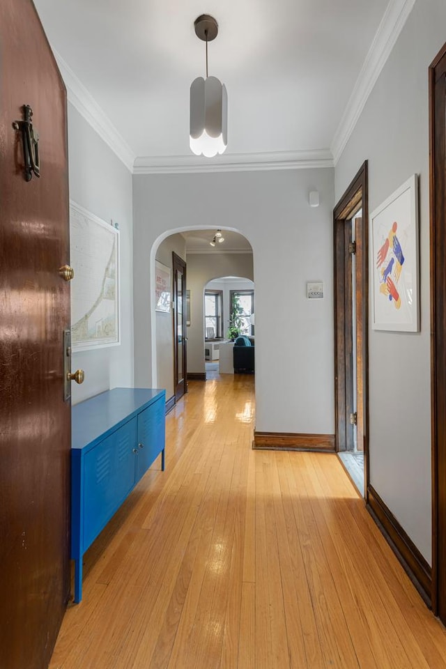 hallway with light wood-type flooring, baseboards, arched walkways, and crown molding