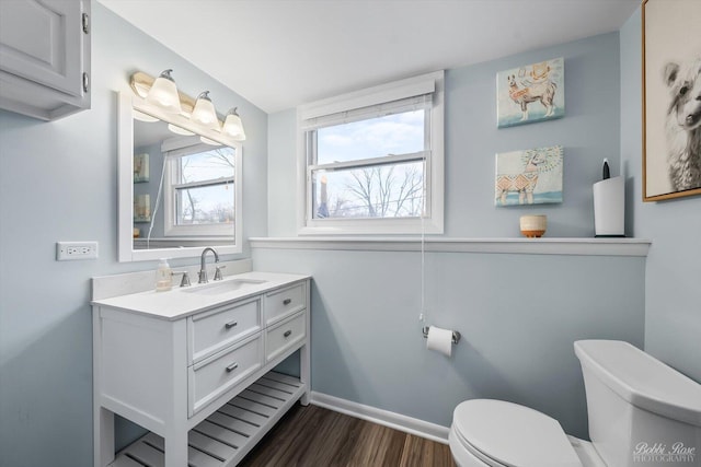 half bath featuring baseboards, vanity, toilet, and wood finished floors