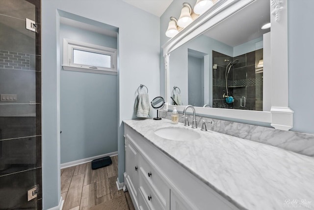 full bath featuring wood tiled floor, tiled shower, vanity, and baseboards