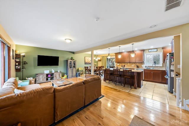 living area with light wood-style floors, visible vents, and a notable chandelier