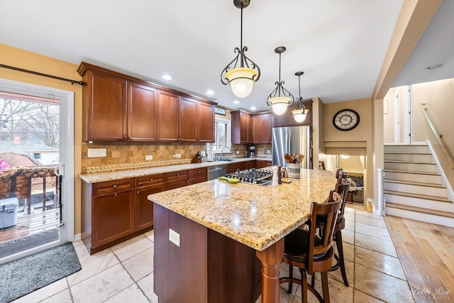 kitchen with stainless steel appliances, a kitchen island, backsplash, and light stone countertops