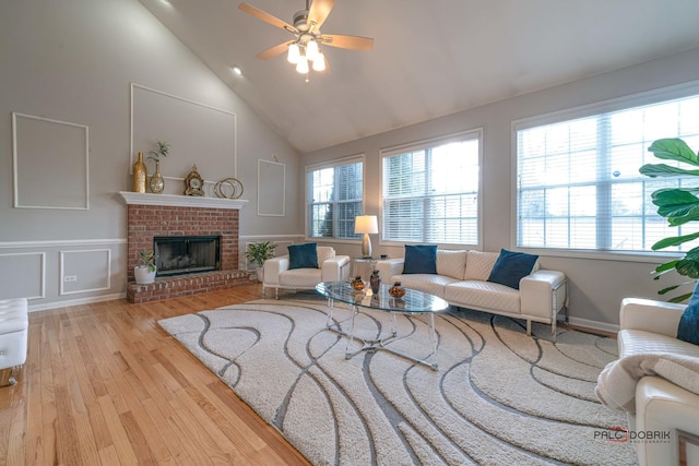 living room with a decorative wall, a brick fireplace, ceiling fan, wood finished floors, and high vaulted ceiling