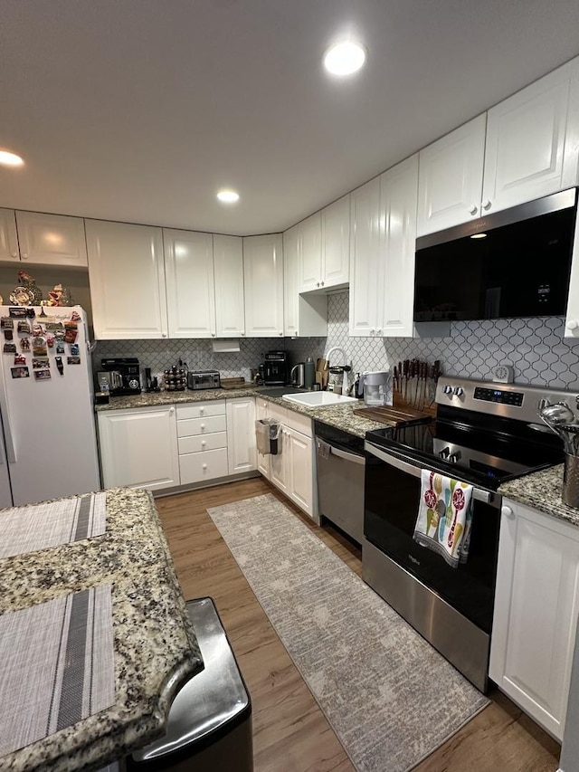 kitchen featuring wood finished floors, a sink, stainless steel appliances, white cabinetry, and backsplash