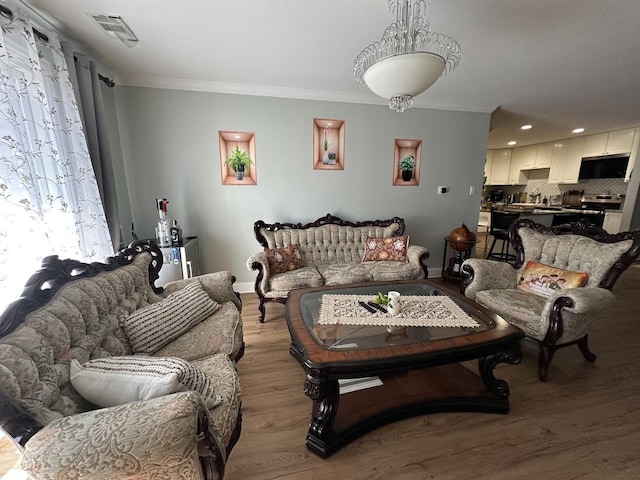 living area with baseboards, light wood-style flooring, visible vents, and crown molding