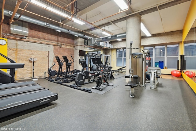 exercise room featuring brick wall and a towering ceiling