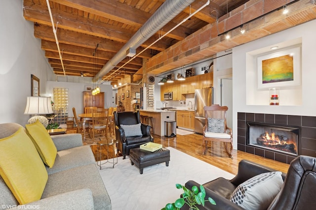 living area featuring light wood-style flooring, wood ceiling, beam ceiling, a tiled fireplace, and track lighting