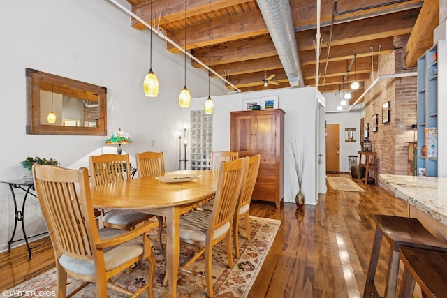 dining space featuring a towering ceiling, brick wall, hardwood / wood-style floors, and beamed ceiling