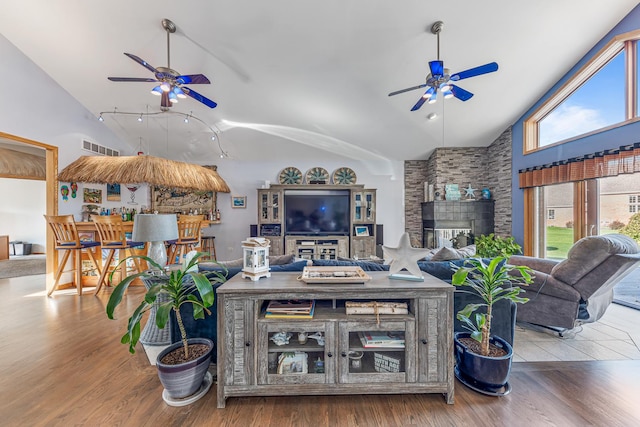 living area with visible vents, a stone fireplace, wood finished floors, and a ceiling fan