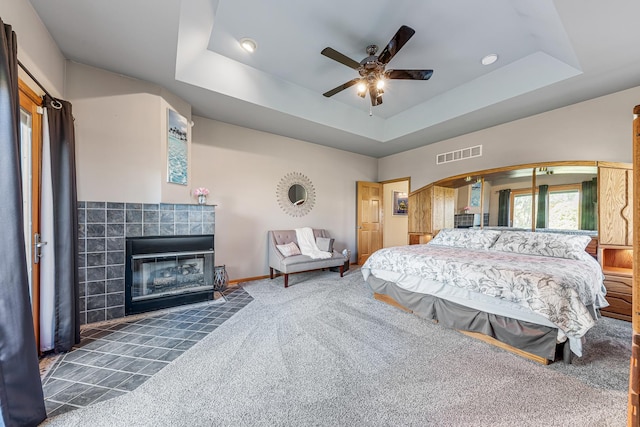 carpeted bedroom featuring arched walkways, a tiled fireplace, a raised ceiling, and visible vents