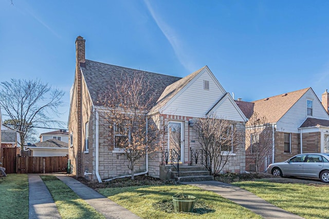 view of front of house with fence, a shingled roof, a chimney, a front lawn, and stone siding