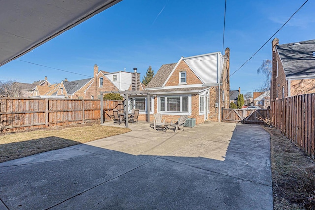 rear view of property featuring brick siding, a fenced backyard, a patio, and a gate