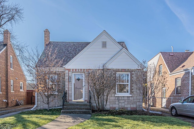 view of front of house featuring a shingled roof, fence, a front yard, a chimney, and stone siding