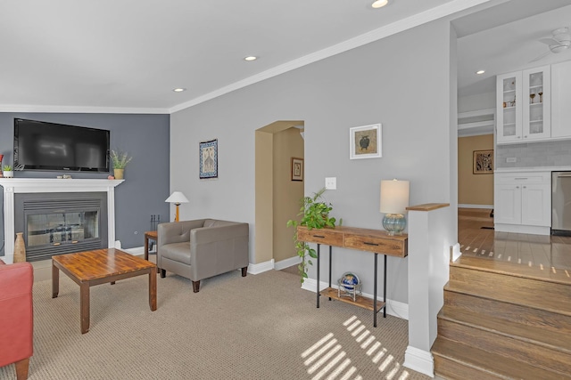 living room featuring ornamental molding, a glass covered fireplace, recessed lighting, carpet, and baseboards