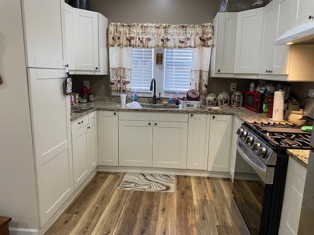 225 W Dakota St, Spring Valley, IL 61362 - kitchen featuring stainless steel range with gas cooktop, a sink, under cabinet range hood, light wood-style flooring, and white cabinets