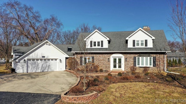 new england style home featuring french doors, brick siding, a shingled roof, a garage, and driveway