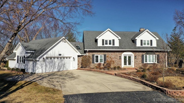 new england style home with french doors, brick siding, driveway, and an attached garage