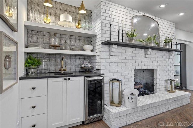 bar featuring beverage cooler, dark wood-type flooring, a brick fireplace, a sink, and recessed lighting