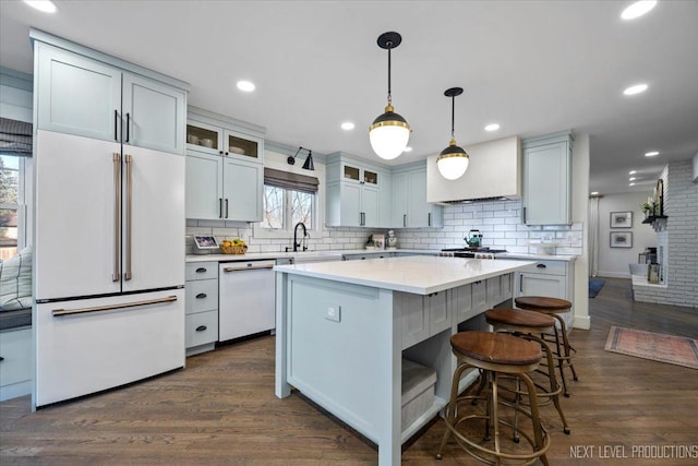 kitchen featuring dark wood-type flooring, glass insert cabinets, a kitchen island, a sink, and white appliances