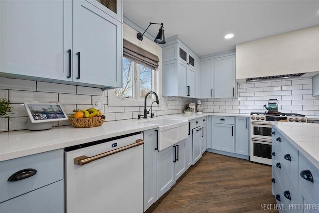 kitchen with range with two ovens, decorative backsplash, dark wood-type flooring, white dishwasher, and a sink