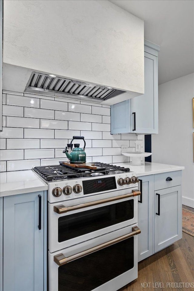 kitchen with light countertops, double oven range, custom range hood, and decorative backsplash