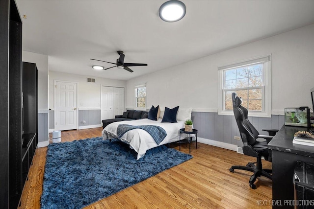 bedroom with wainscoting, wood finished floors, visible vents, and a ceiling fan