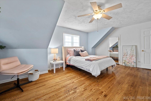 bedroom with lofted ceiling, a ceiling fan, a textured ceiling, wood finished floors, and baseboards