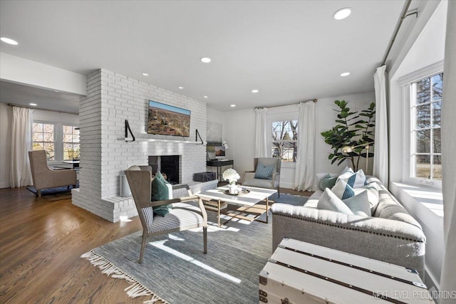 living area with recessed lighting, a brick fireplace, and wood finished floors