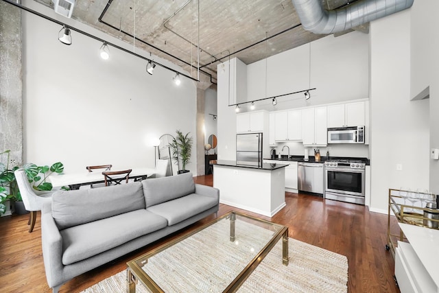 interior space with dark wood-type flooring, a high ceiling, appliances with stainless steel finishes, dark countertops, and rail lighting