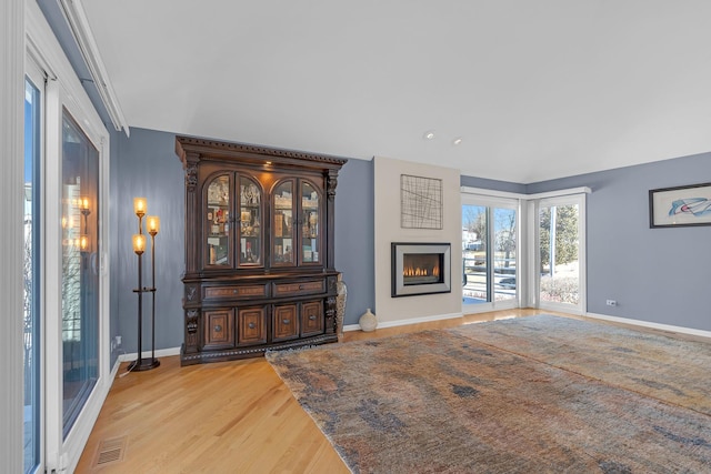 living area with visible vents, baseboards, light wood-style floors, and a lit fireplace