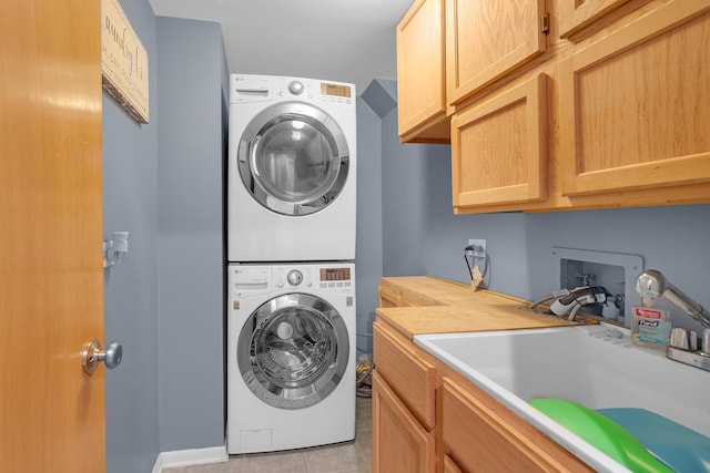 clothes washing area featuring a sink, light tile patterned flooring, and stacked washing maching and dryer