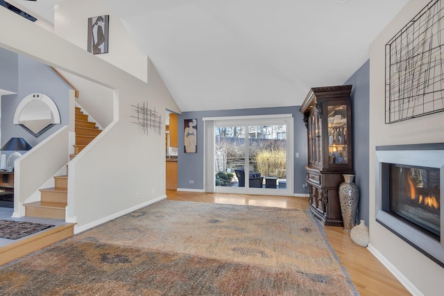 living room with a glass covered fireplace, stairway, wood finished floors, and baseboards