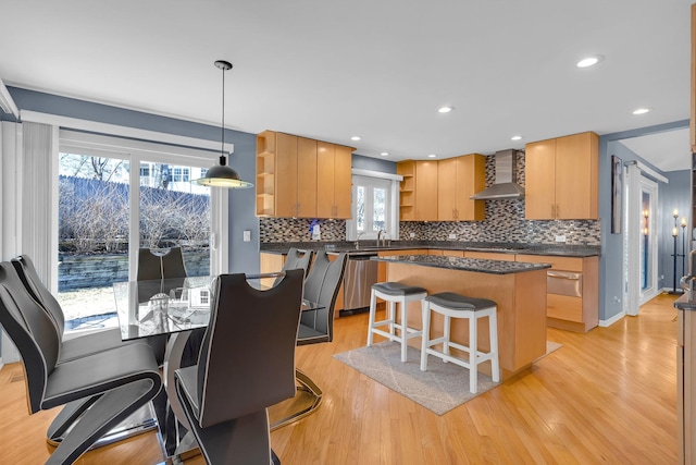 kitchen with dark countertops, open shelves, light wood-style floors, wall chimney exhaust hood, and stainless steel dishwasher