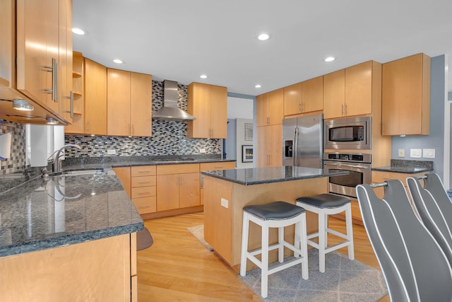 kitchen with a sink, stainless steel appliances, light wood-style floors, and wall chimney exhaust hood